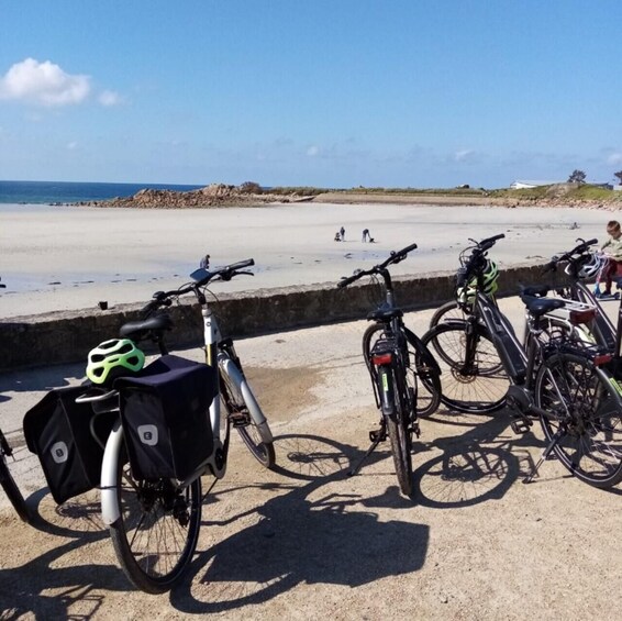 Bicycles parked on a concrete surface near a sandy beach with people in the distance. 4