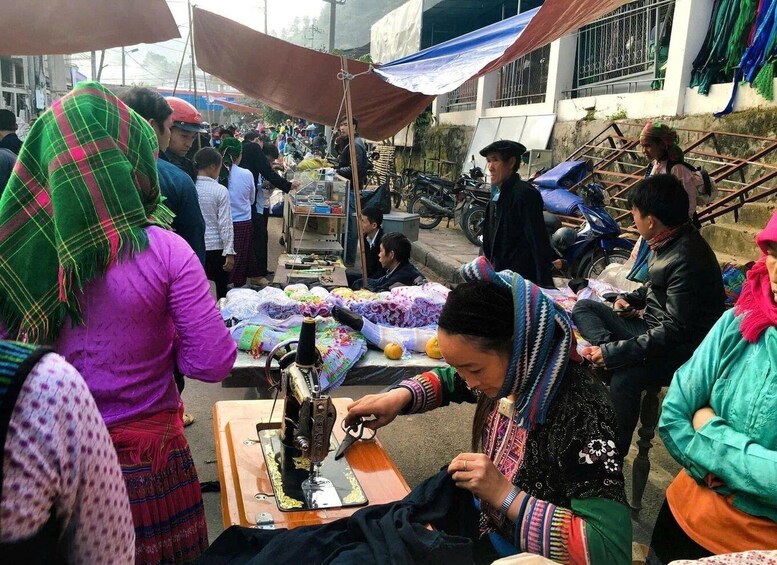 A bustling outdoor market with people engaged in various activities, including sewing and selling goods. 5