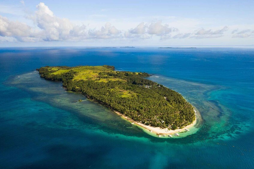 An aerial view of a tropical island with clear turquoise waters, dense green vegetation, and a sandy beach. 2