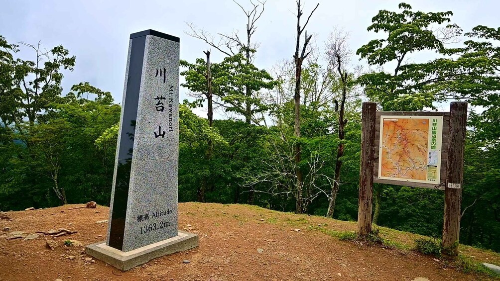 A stone monument with Japanese inscriptions, a dirt path, and a map sign in a forested area. 3