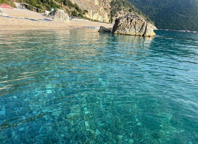 Clear turquoise water with visible rocks and a rocky outcrop near a beach. 3