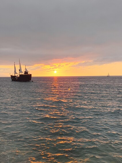 A sunset over the ocean with a large ship and a sailboat. 2