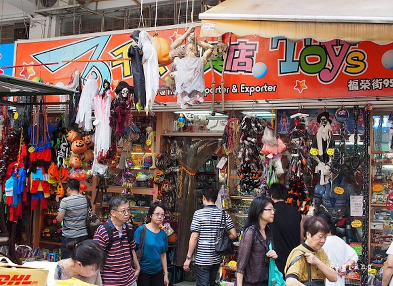 A busy street market with various stalls selling toys and Halloween decorations. 5