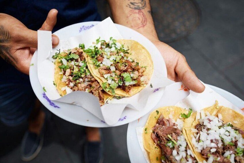 A person holding two plates of tacos with shredded meat and diced onions. 1
