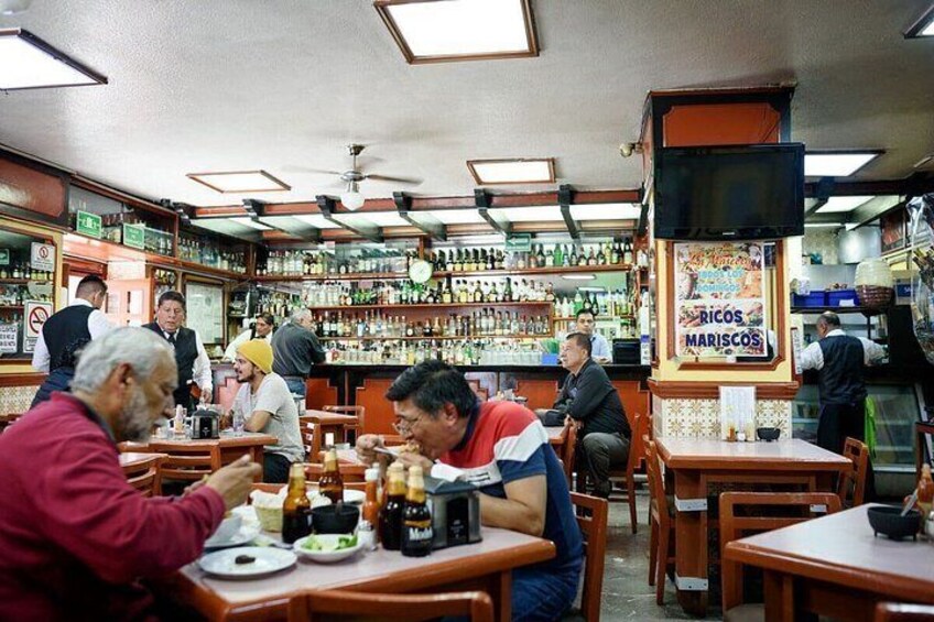 A restaurant interior with wooden tables, chairs, and a bar area with bottles. 5