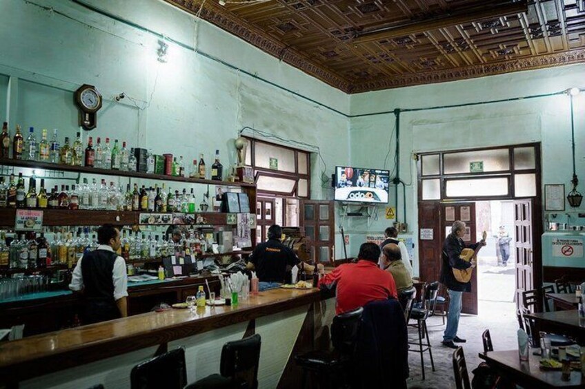 A bar with shelves of bottles, a television, and a clock on the wall. 5