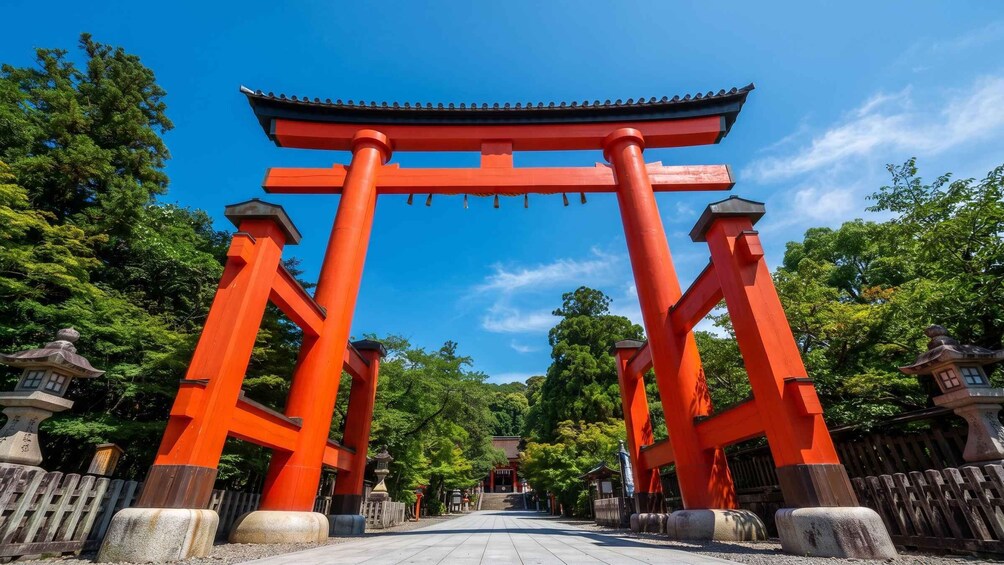 A traditional Japanese torii gate with red pillars and a tiled roof, surrounded by lush greenery and a clear blue sky. 3