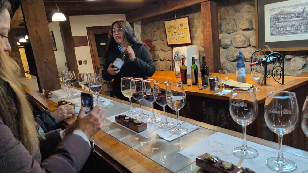 A wine tasting event with glasses of red wine on the counter and a person holding a bottle. 2