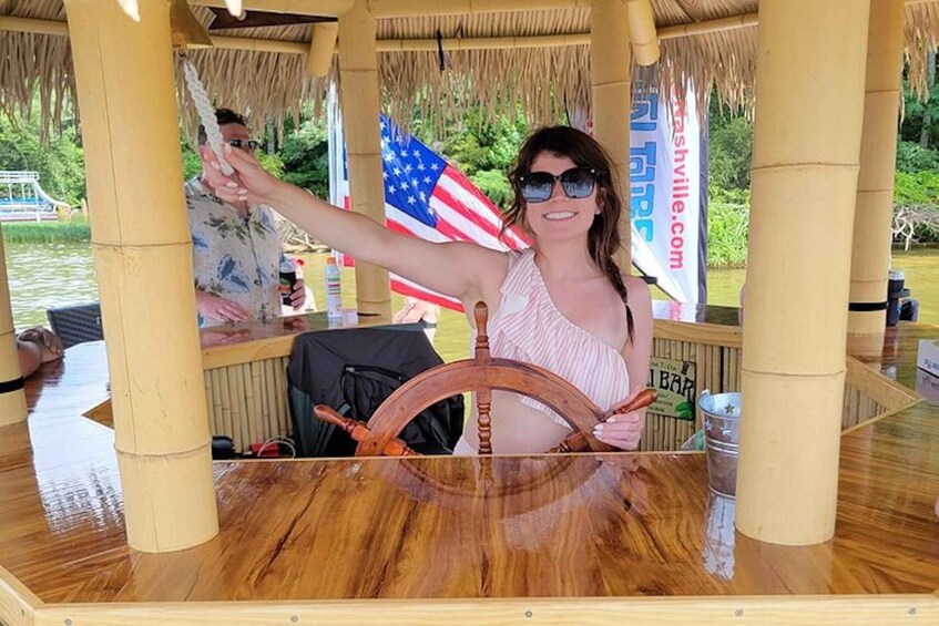 A person steering a wooden boat with an American flag in the background. 1