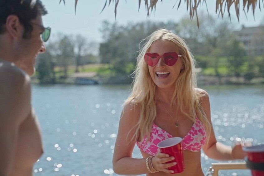A person in a pink bikini holding a red cup by a body of water with trees and a building in the background. 4