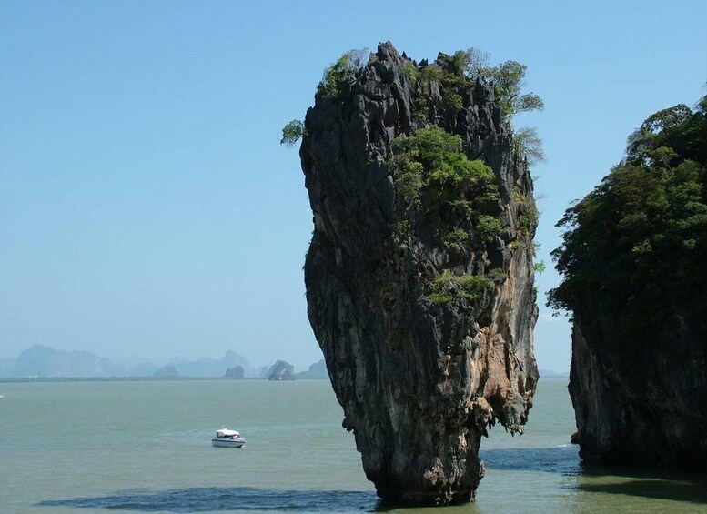 A large rock formation surrounded by water with a boat in the distance. 1