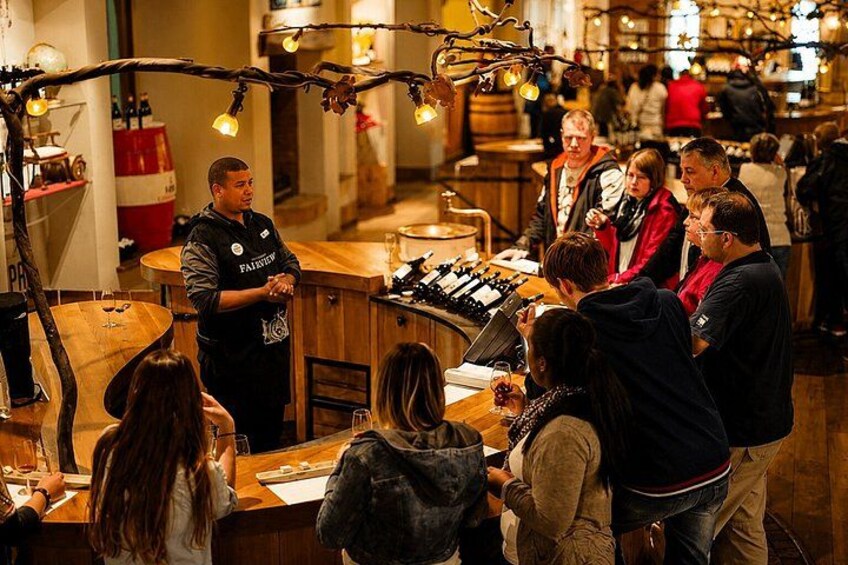 A wine tasting event with a server, wine bottles, and guests seated at tables. 2
