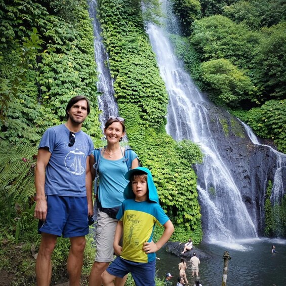 A family standing in front of a waterfall surrounded by lush greenery. 3