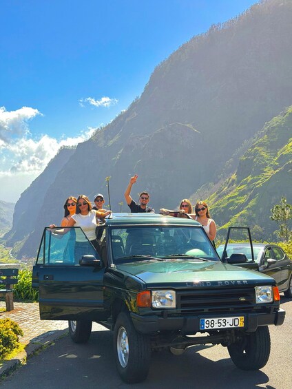 A group of people in a green Land Rover on a mountain road with a clear sky and green hills in the background. 1