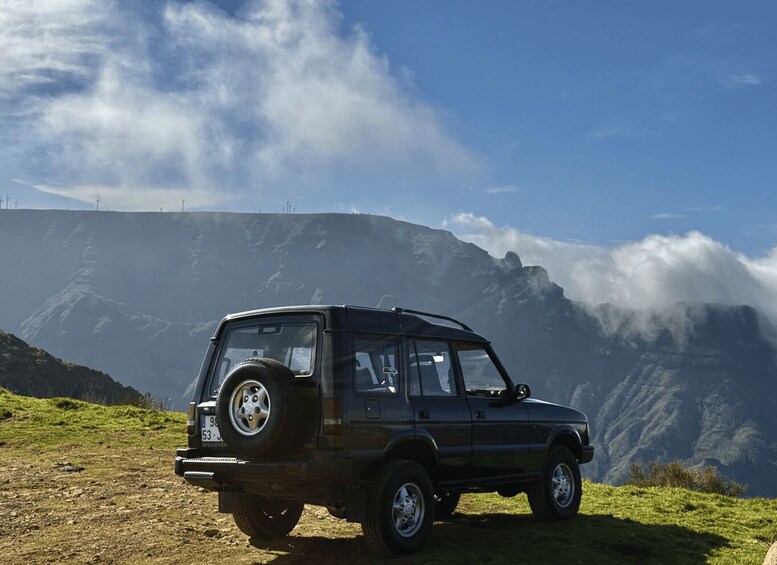 A black SUV parked on a grassy hill with a mountainous backdrop and clouds. 3