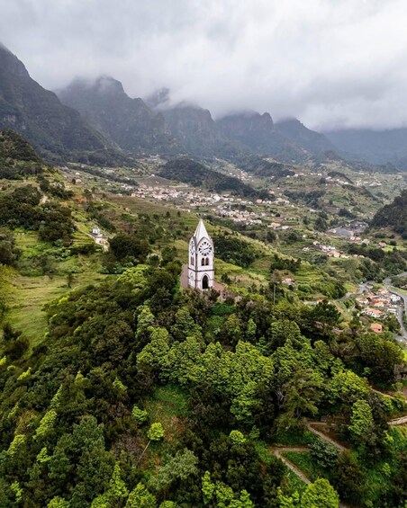 A white church with a clock tower surrounded by lush green hills and a village in the valley below. 4
