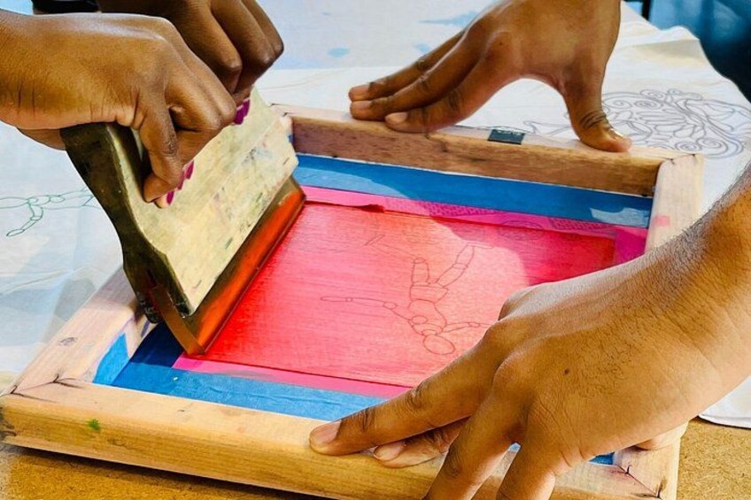 Hands using a wooden press on a red and blue framed surface with a drawing. 2