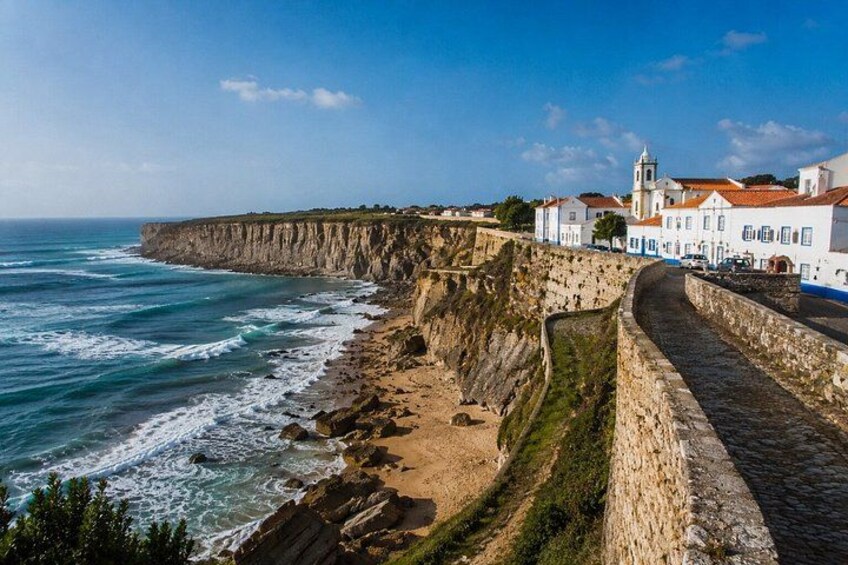 A coastal town with a fortified wall, ocean waves, and white buildings with red roofs. 5