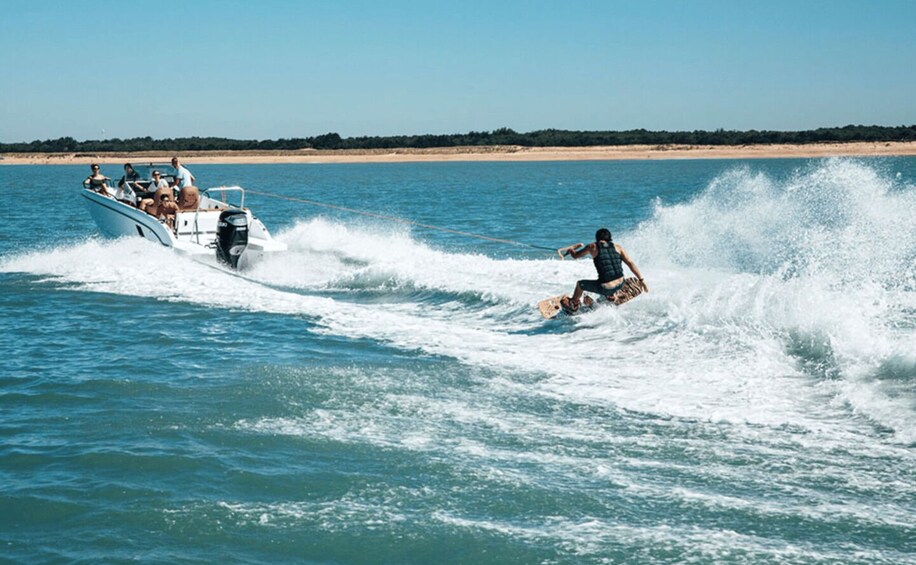 A person wakeboarding behind a boat on a body of water with a beach in the background. 2