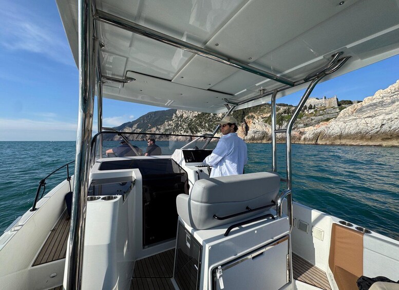 A boat with two people on deck, rocky coastline in the background, and calm sea. 1
