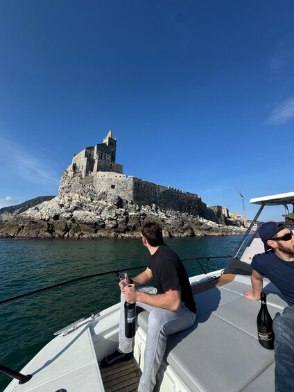 A boat with two people, one holding a bottle, and a castle on a rocky island in the background. 3