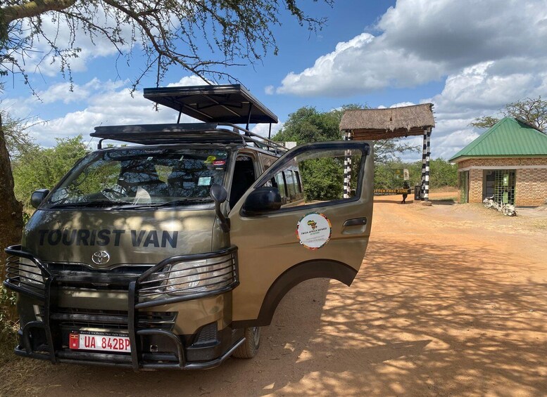 A tourist van parked in a natural setting with a thatched-roof building and a green-roofed structure in the background. 5