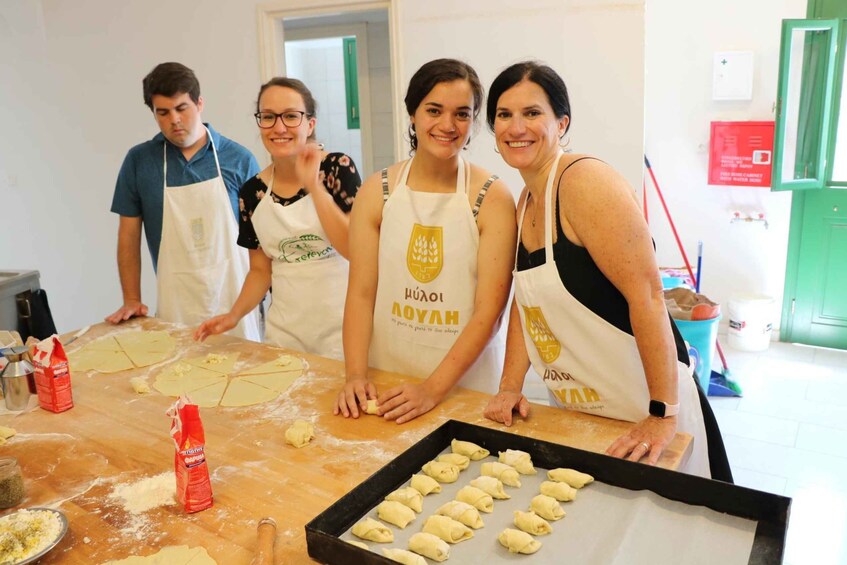 Four people wearing aprons, preparing food on a table with flour and dough. 1