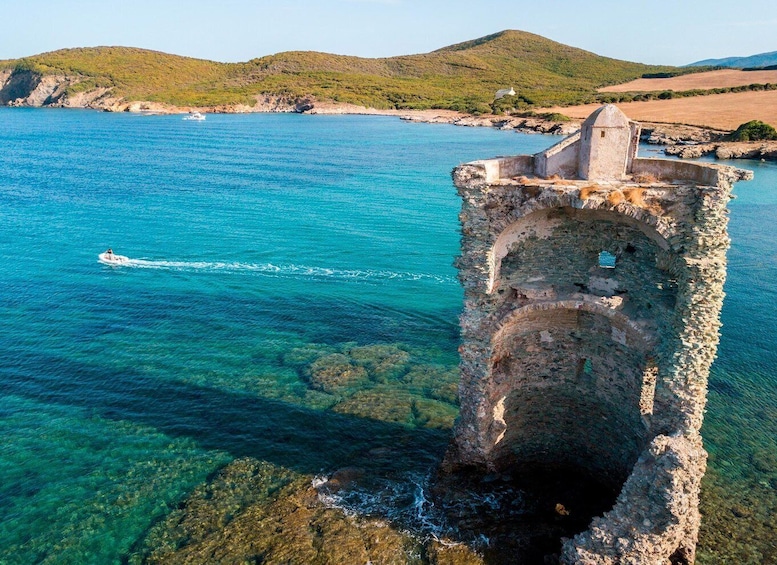 A coastal landscape with a clear blue sea, a rocky structure, and distant hills. 1