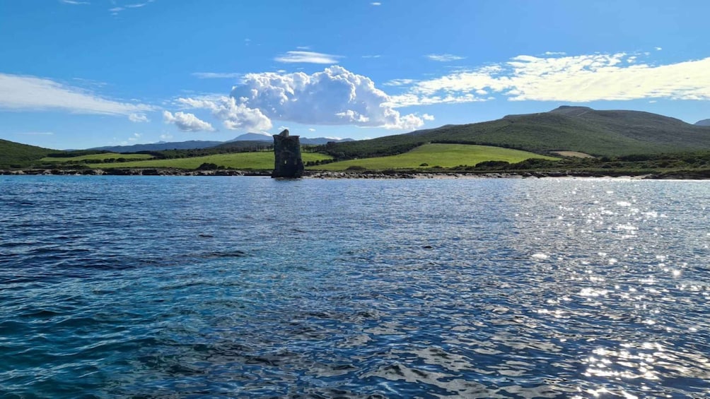 A coastal landscape with a stone structure in the water, green hills, and a partly cloudy sky. 4