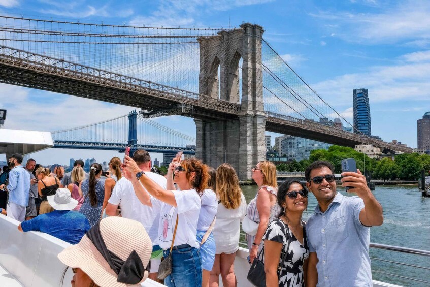 A group of people taking a selfie with the Brooklyn Bridge in the background. 1