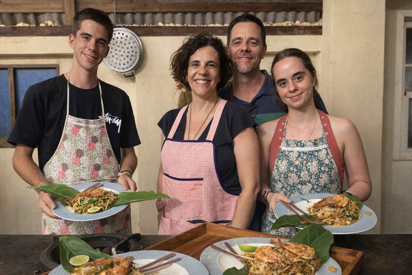 Four people holding plates of food, wearing aprons, in a kitchen setting. 2