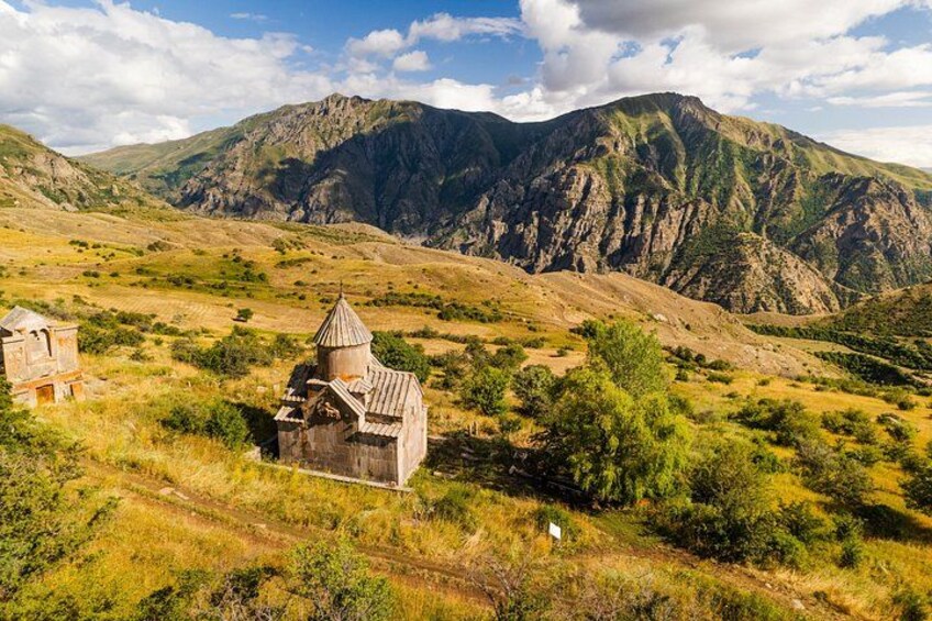 A rural landscape with a small church, rolling hills, and mountains in the background. 4