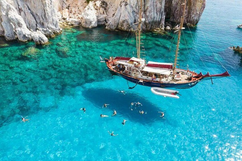 A boat anchored in clear turquoise waters with rocky cliffs in the background. 2
