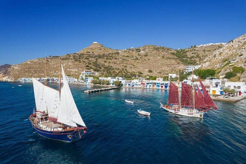 A coastal scene with sailboats, a small harbor, and white buildings on a hillside. 1