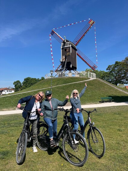 Three people on bicycles in front of a windmill. 4