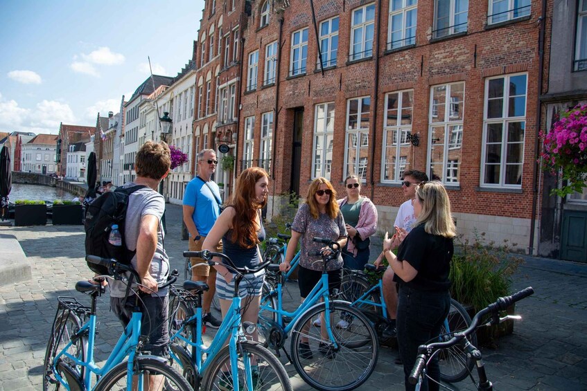 A group of people standing around bicycles on a cobblestone street in front of a row of red brick buildings. 2