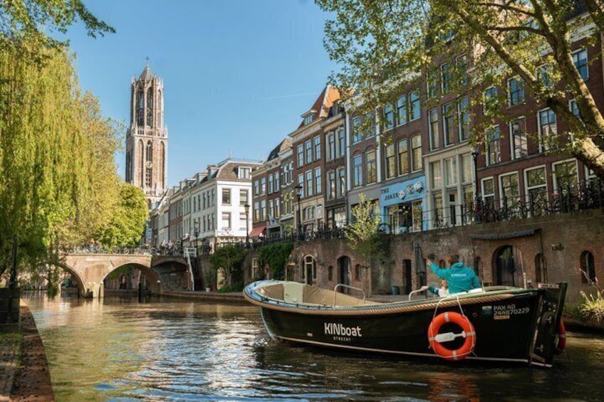 A boat named 'KINOboat' on a canal, a bridge, and historic buildings in the background. 1