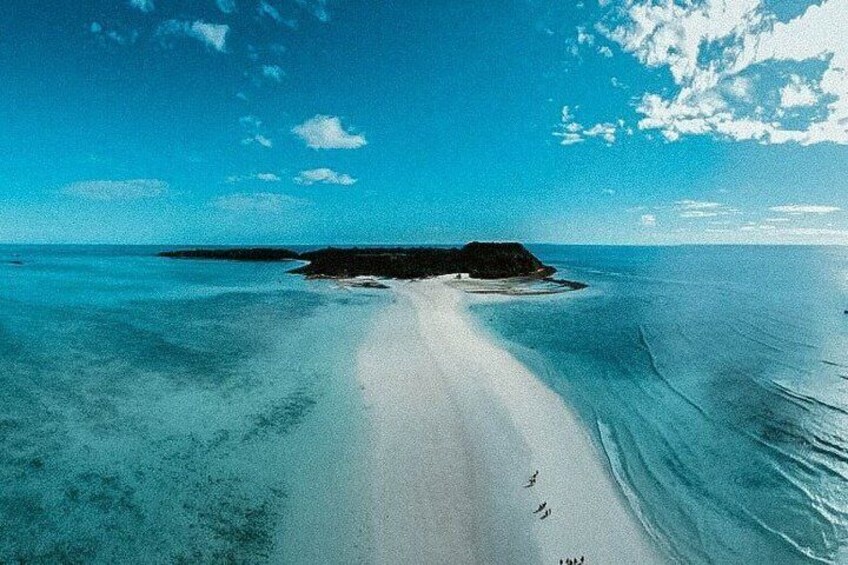A beach with clear turquoise water, a sandy path, and a small island in the distance. 4