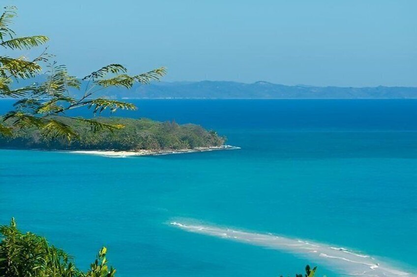 A coastal landscape with clear blue waters, a sandy beach, and a distant island. 5