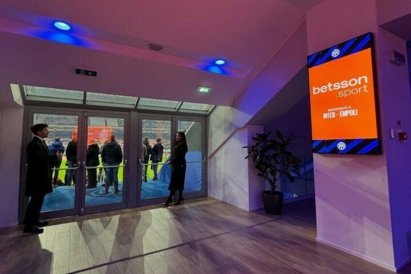 An indoor sports facility with glass doors, a Betsson advertisement, and a potted plant. 3