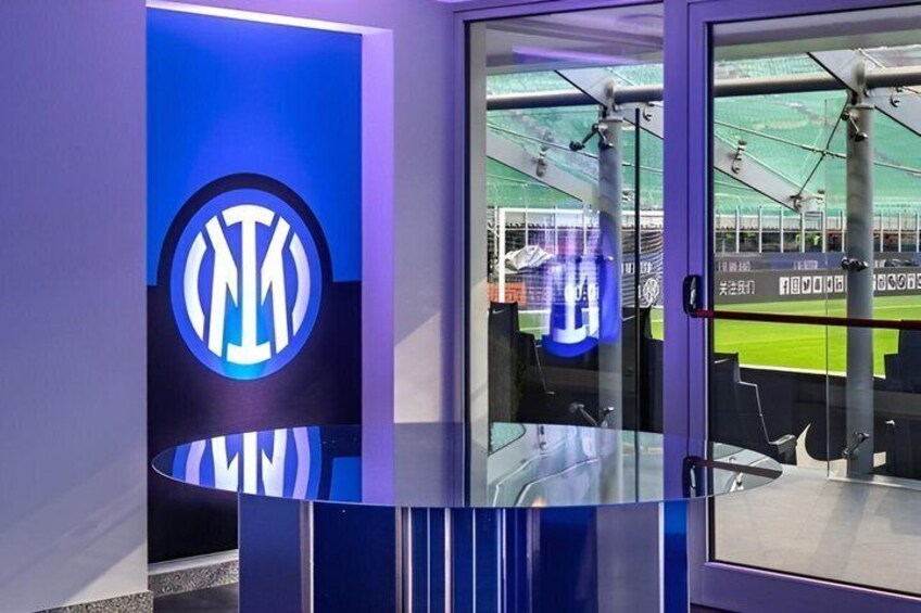 A sports facility with a prominent logo, a glass barrier, and a seating area. 1