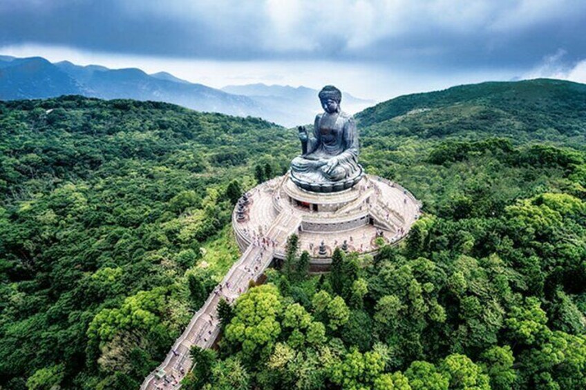 A large Buddha statue surrounded by lush greenery and mountains. 2