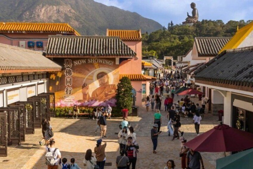 A traditional street with people walking, a large Buddha statue in the background, and a sign that says 'NOW SHOWING!' 5