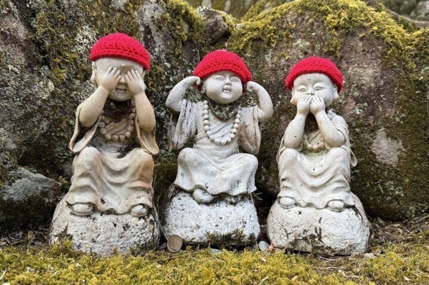 Three stone statues with red hats sitting on mossy ground. 3
