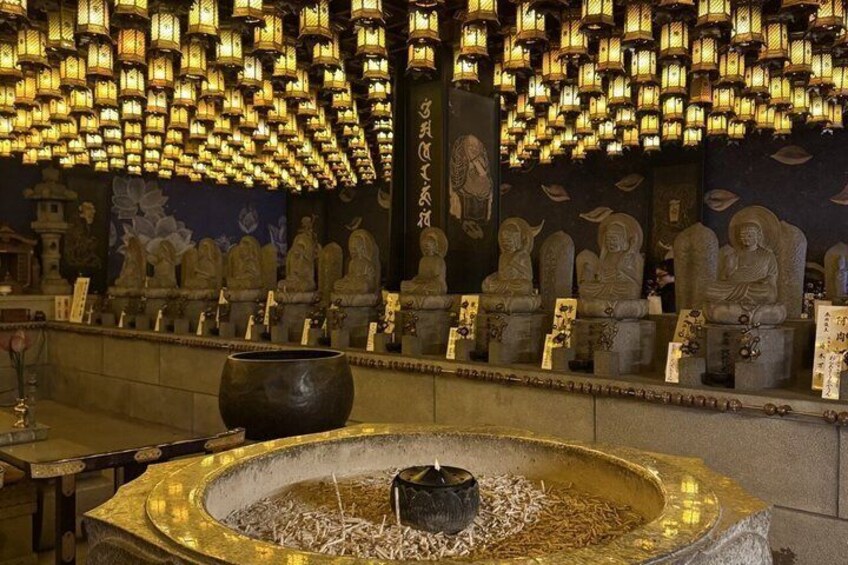 A temple interior with stone statues, a large incense burner, and hanging lanterns. 2