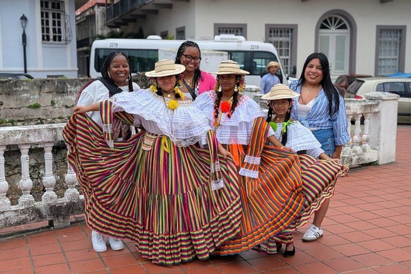 A group of people in traditional colorful dresses, a stone wall, and a building in the background. 4