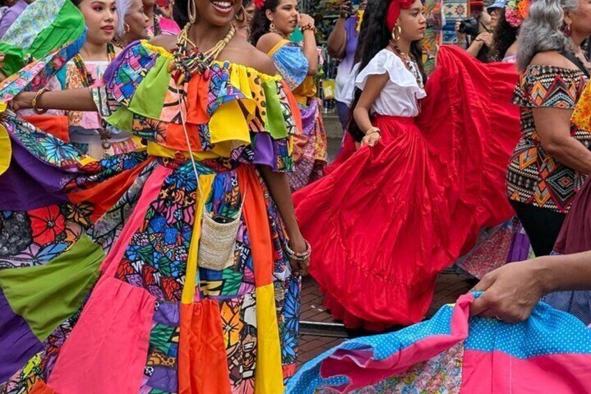 A person in a colorful traditional dress with a red skirt, surrounded by others in a festive outdoor setting. 5