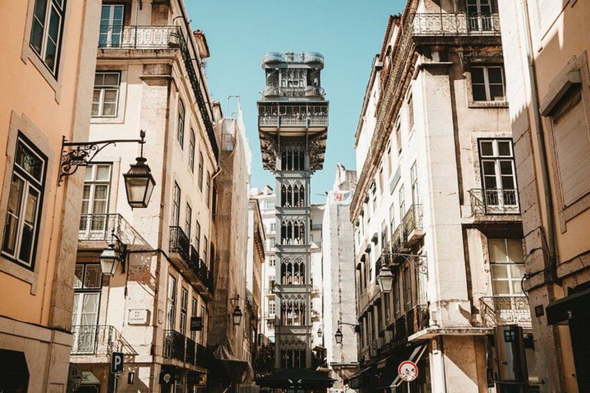 A narrow street flanked by historic buildings with ornate facades and a prominent tower structure in the center. 3