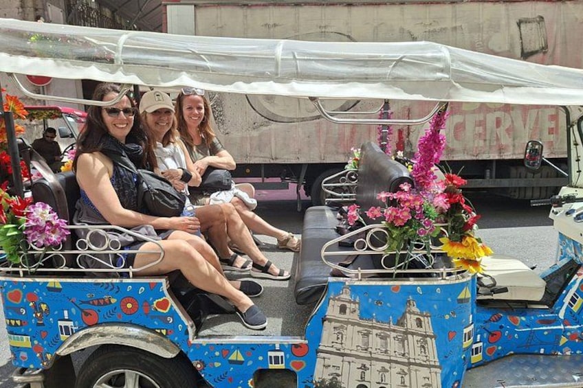 A colorful, decorated cart with passengers, a truck in the background, and a building with a dome. 4