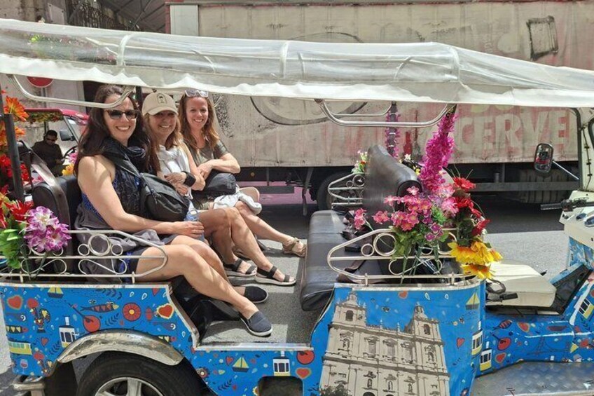 A colorful, decorated cart with passengers, a truck in the background, and a building with a dome. 4